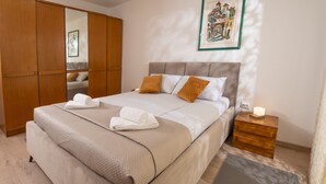 Quarto com uma cama, um guarda-roupa de madeira, uma mesa de cabeceira com abajur e um quadro pendurado na parede.