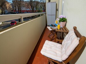 Ein Balkon mit einem Holzstuhl und einem kleinen Tisch, einem Blumentopf und einem Glas Orangensaft.