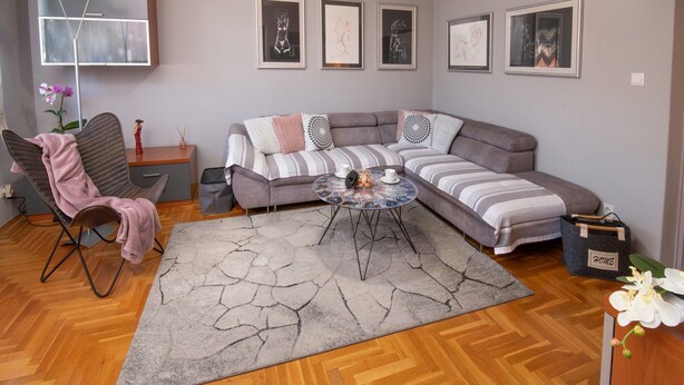 Uma sala de estar moderna com um sofá cinzento, uma mesa de centro estampada e um tapete cinza.