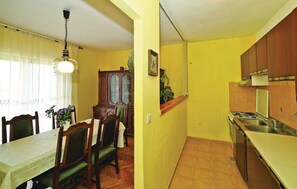 A compact kitchen with a gas stove and sink, a dining area with a table and chairs, and a hanging light fixture. - Apartments Halilovic - Two Bedroom Apartment 1 (Trogir)