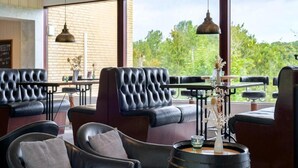 Ett modernt loungeområde med lädersoffor, ett träfat och stora fönster med utsikt över grönområden.