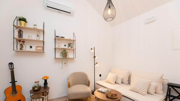Una sala de estar con un sofá, una silla, una mesita, una guitarra y una lámpara de pie.