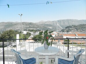 A balcony with a table and chairs, overlooking a mountainous landscape with a bridge in the distance. - Guest House Bridge View - Double Room With Balcony and Sea View (Dubrovnik)