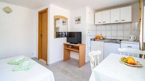 Ett kompakt hotellrum med en enkel s äng, ett skrivbord med en tv, ett litet pentry och en matplats med ett bord dukat för två personer.