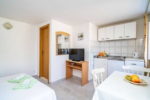 Ein kompaktes Hotelzimmer mit einem Einzelbett, einem Schreibtisch mit Fernseher, einer kleinen Küchenzeile und einer Essecke für zwei Personen.