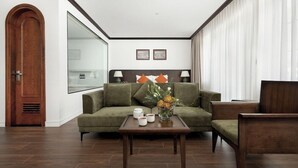 A modern hotel room with a green sofa, a wooden coffee table, and a view of the city through large windows. - Bach Dang Hotel (Hai Phong)