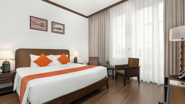 A hotel room with a large bed, two bedside tables, a chair, a desk, and a lamp. - Bach Dang Hotel (Hai Phong)