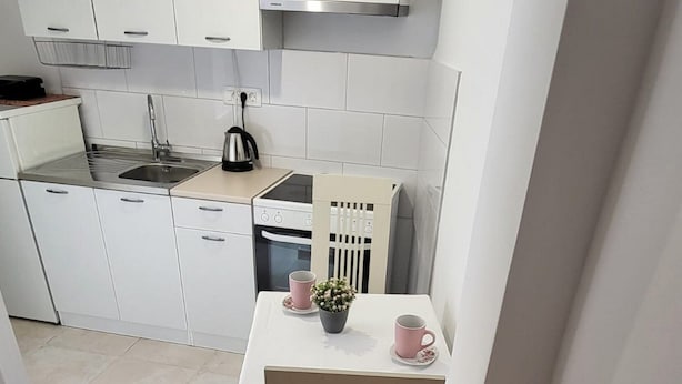 Ett litet kök med vita skåp, en spis och ett bord med en stol.
