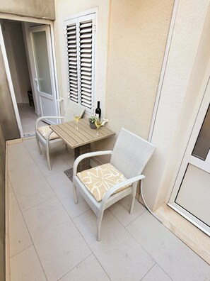 Eine kleine Terrasse im Freien mit Tisch, zwei Korbstühlen, einer Weinflasche und einem Blumentopf.