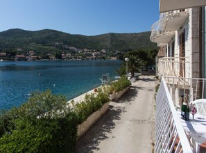 A balcony with a view of a calm body of water, a pathway, and a row of houses in the background. - Villa Malfi - Standard Double Room With Sea View (Dubrovnik)