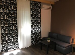 Ein Wohnzimmer mit einer Couch, einem kleinen Tisch mit einer Pflanze und einem Fenster mit Vorhängen.