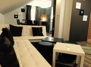 Ein modernes Wohnzimmer mit einem weißen Sofa, schwarzen Kissen, einem kleinen weißen Tisch und einem dunklen Boden.