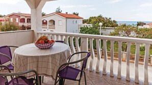 Uma varanda com mesa e cadeiras, uma tigela de frutas e vista para as casas e o mar.
