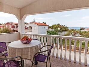 A balcony with a table and chairs, a bowl of fruit, and a view of houses and the sea. - Apartments Hak - Two Bedroom Apartment With Terrace and Sea View (Vir)