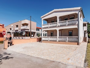 A two-story building with a balcony, a stop sign, and a stone-paved area. - Apartments Hak - Two Bedroom Apartment With Terrace and Sea View (Vir)