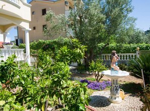 A garden with a fountain, trees, and a white building with balconies. - Mobile Homes Bella Vita 1 (Biograd na Moru)