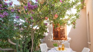Un'area salotto esterna con un tavolo apparecchiato per due, circondata da vegetazione lussureggiante e alberi in fiore.