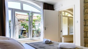Habitación de hotel con cama, ventana con cortinas, puerta que da a otra habitación y vistas al exterior.