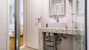 Un baño moderno con cabina de ducha de vidrio, lavamanos blanco y salpicadero de azulejos.