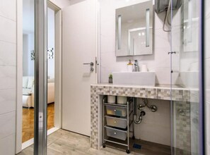 Ein modernes Badezimmer mit Duschkabine aus Glas, Waschbecken in Weiß und einer gefliesten Rückwand.