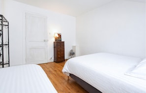 Une chambre avec deux lits, une commode en bois, un radiateur et une porte.