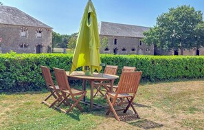 An outdoor seating area with a table and chairs, a yellow umbrella, and a hedge in the background. - Au c?ur des sites du D-Day (Géfosse-Fontenay)