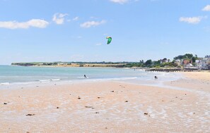 Une plage avec une jetée qui s’avance dans l’eau, un ciel dégagé et une personne qui fait voler un cerf-volant.
