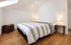 A bedroom with a bed, bedside lamps, a wooden floor, a small table, and a decorative trunk. - Au c?ur des sites du D-Day (Géfosse-Fontenay)