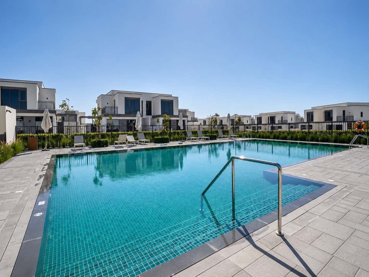 A swimming pool with a tiled edge, surrounded by lounge chairs and a fence.