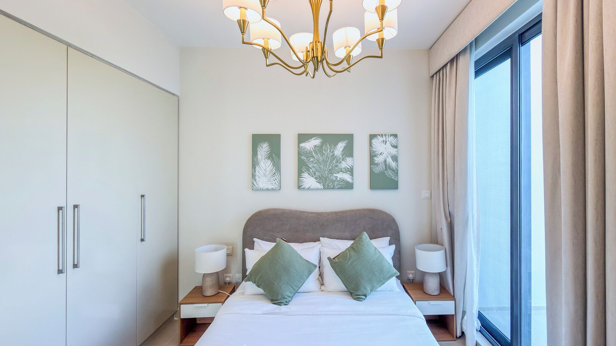 A hotel room with a bed, bedside tables, a chandelier, and artwork on the wall.