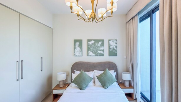 Ett hotellrum med en säng, sängbord, en kristallkrona och konstverk på väggen.