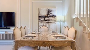 Un coin repas avec une longue table dressée pour six personnes, entourée de chaises, un tableau au mur, un téléviseur et un escalier.