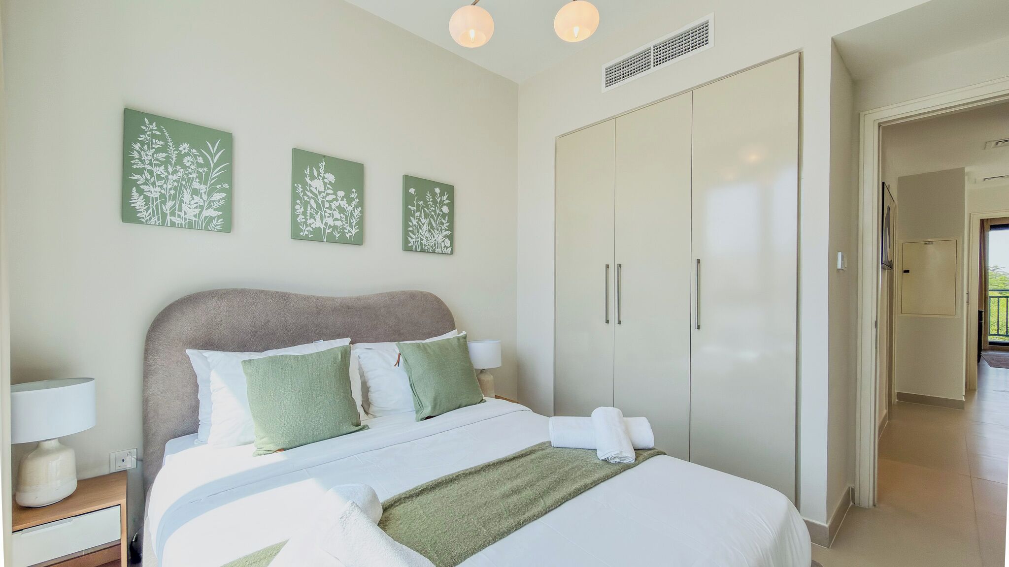 Un dormitorio con cama, mesitas de noche, armario y cuadros en la pared.