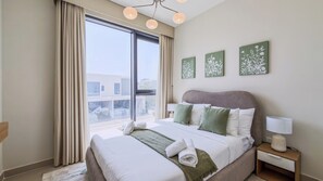 Une chambre d’hôtel avec un grand lit, une table de chevet, une lampe et une vue sur l’extérieur.