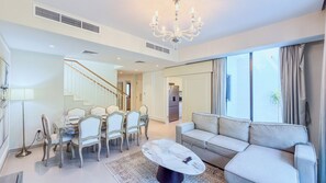 A spacious living area with a dining table set for six, a sofa, and a chandelier. - Maple Residences - Dubai Hills Estate (Dubai)
