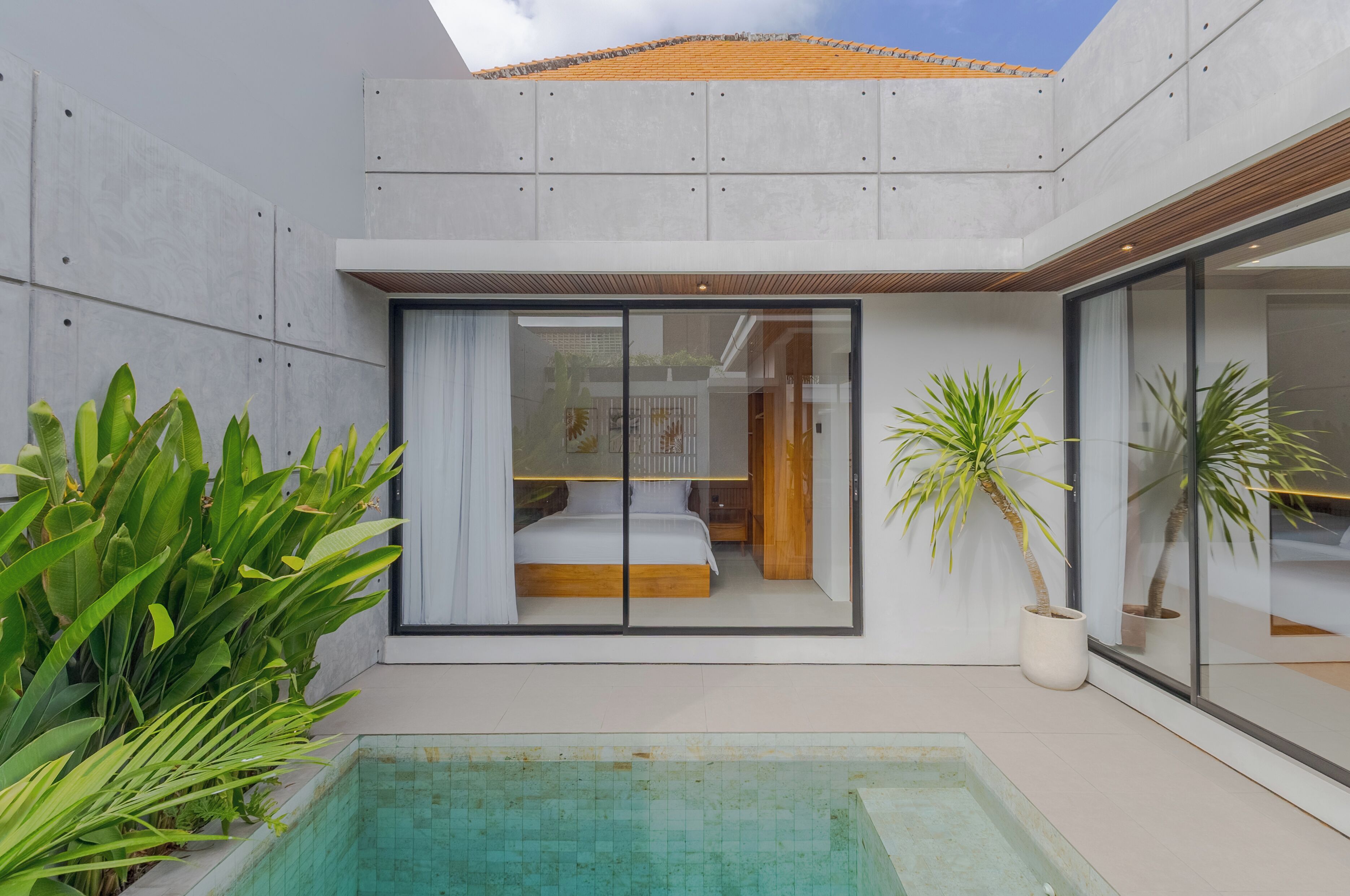 Ein modernes Haus mit einem verglasten Schlafzimmer, einem Swimmingpool und tropischen Pflanzen.