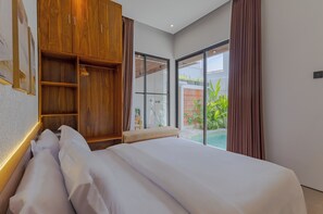 A modern bedroom with a large bed, wooden wardrobe, and a sliding glass door leading to a balcony with greenery. - Villa Kartal Bahce by Pertama Stay (Badung Regency)
