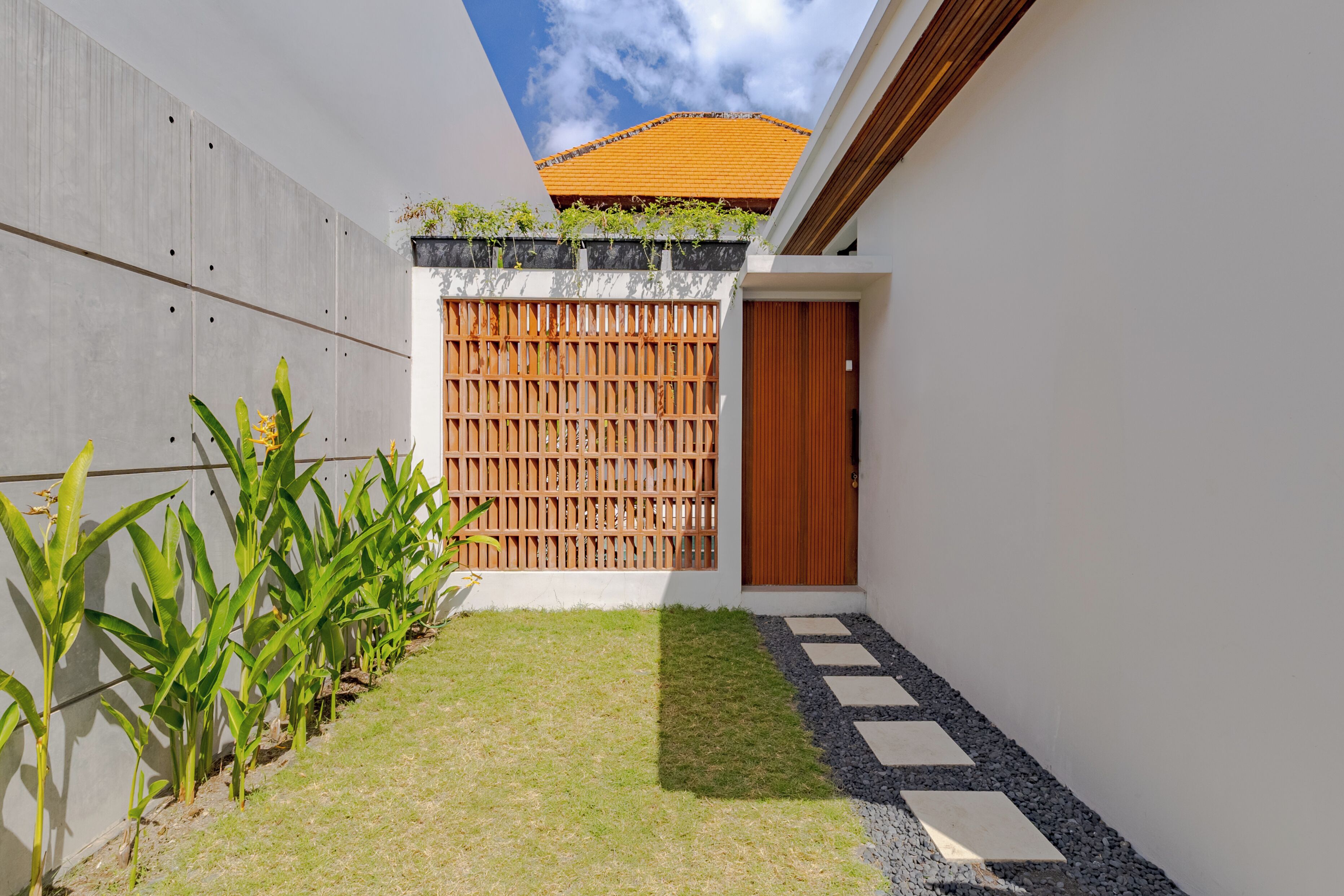 A modern house with a wooden gate, a small garden with grass and plants, and a pathway leading to a door.