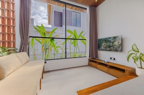 Un salon moderne avec un canapé, un meuble TV en bois, une grande fenêtre donnant sur un paysage verdoyant et un tableau accroché au mur.