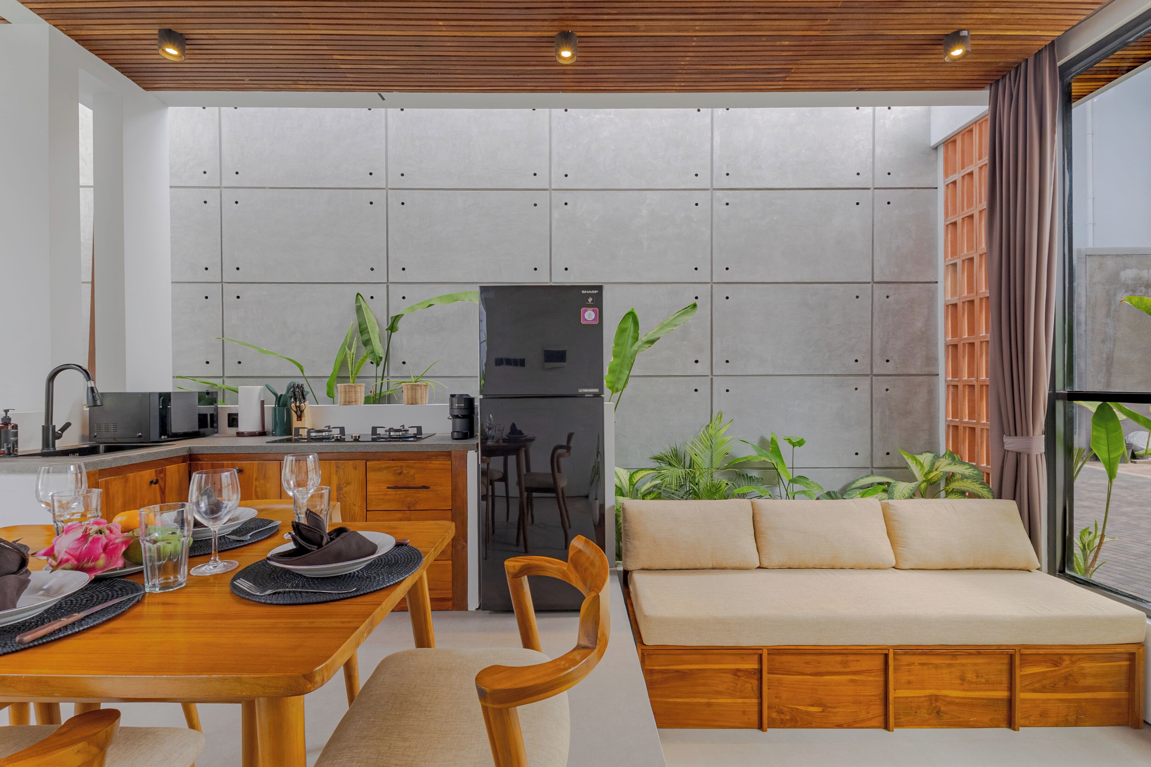 A modern kitchen with a dining area, a sofa, and a view of the outdoors.