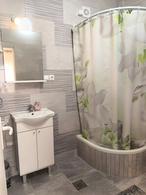 Ein Badezimmer mit weißem Waschbecken, Spiegel und einer Duschvorhang mit floralem Muster.