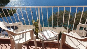 A balcony with two white plastic chairs and a small table, overlooking a calm sea with boats and a hilly landscape in the distance. - Villa Malfi-studio Apartment With Balcony and Sea View (Dubrovnik)