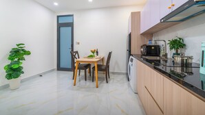 A modern kitchen with a built-in microwave, a dishwasher, and a sink. There is a dining table with chairs and a small potted plant. - LINH KHANG 2 APARTMENT DA NANG (Da Nang)