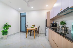 Una cocina moderna con microondas integrado, lavavajillas y fregadero. Hay una mesa de comedor con sillas y una pequeña planta en maceta.