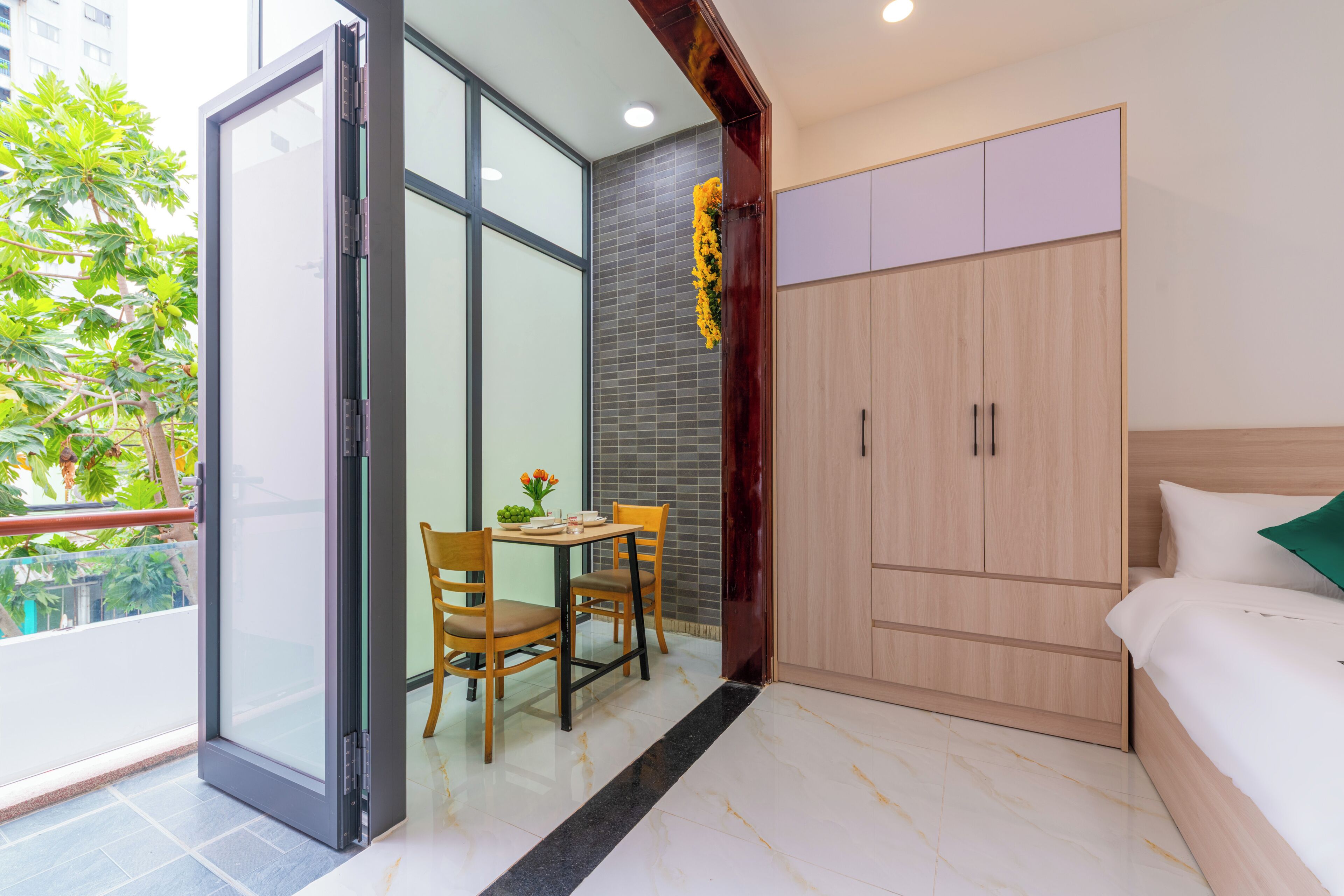 Habitación de hotel con puerta corrediza de vidrio, una mesa de madera con sillas, una cama con ropa blanca y un armario.