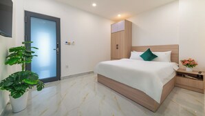 A modern bedroom with a bed, bedside table, and a potted plant. - LINH KHANG 2 APARTMENT DA NANG (Da Nang)