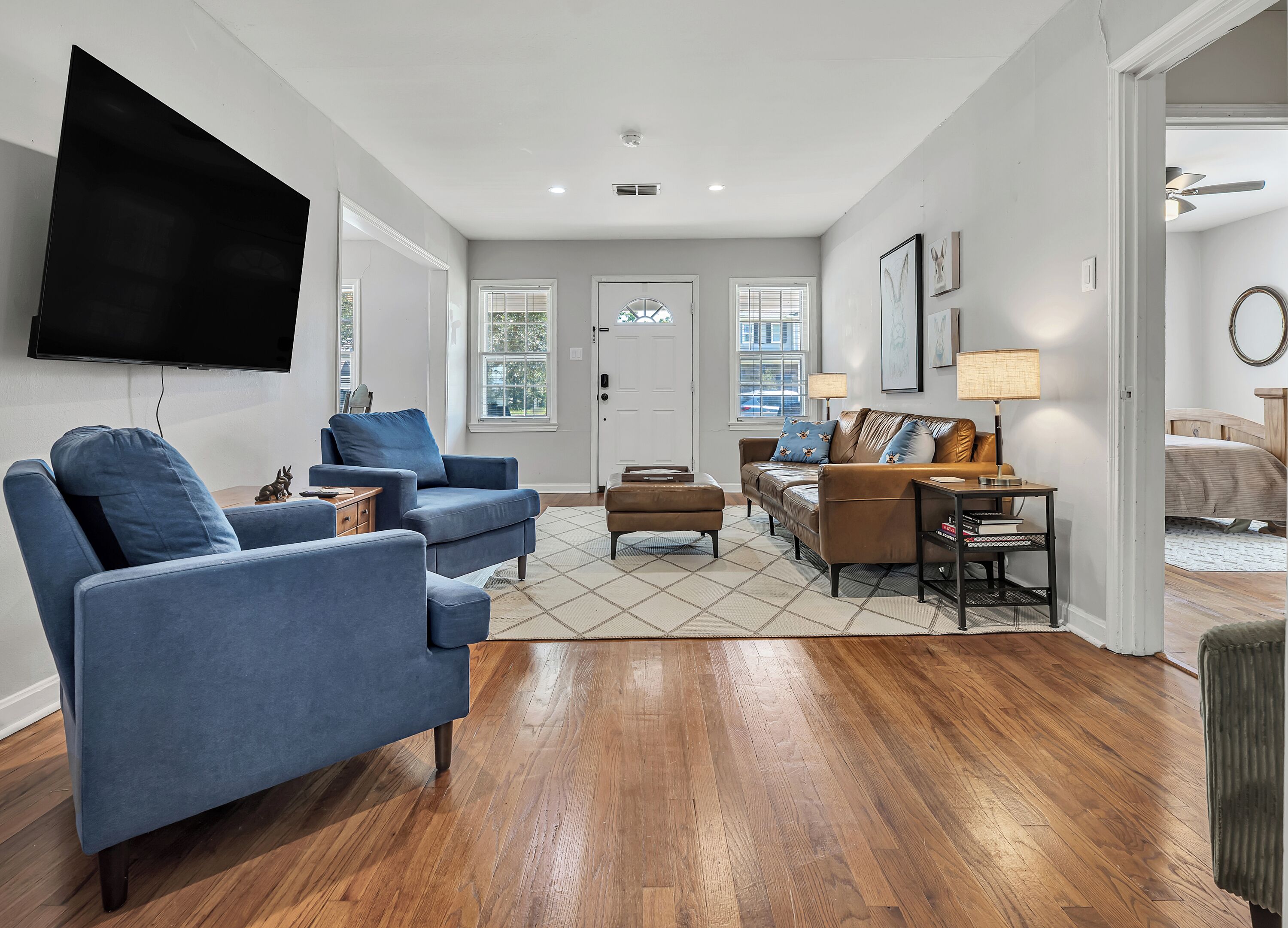 A living room with a flat-screen TV, blue armchairs, a brown sofa, and a wooden floor.