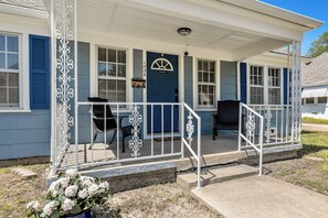 A two-story house with a covered porch, a blue door, and a small garden with white flowers. - Watership Down: 45 Seconds from Texas A&M Campus (College Station)