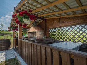 Ein Außenbereich mit Grillplatz, Backofen aus Ziegeln, Holzdeck und hängenden Blumenkörben.
