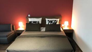 Una cama con cabecera, dos mesitas de noche con lámparas, un sofá gris y una pared roja.
